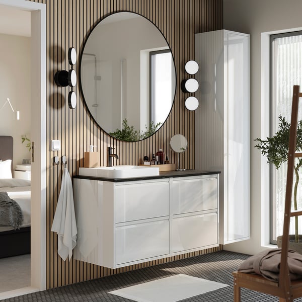 Modern bathroom with white ÄNGSJÖN vanity, marble sink, round mirror, tall cabinet, and black plant.