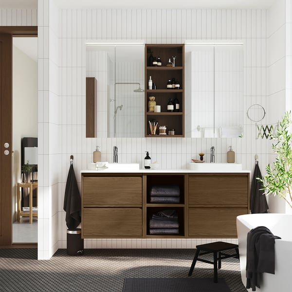 Brown oak bathroom vanity with open/closed storage, double basin, towels, and mirror.