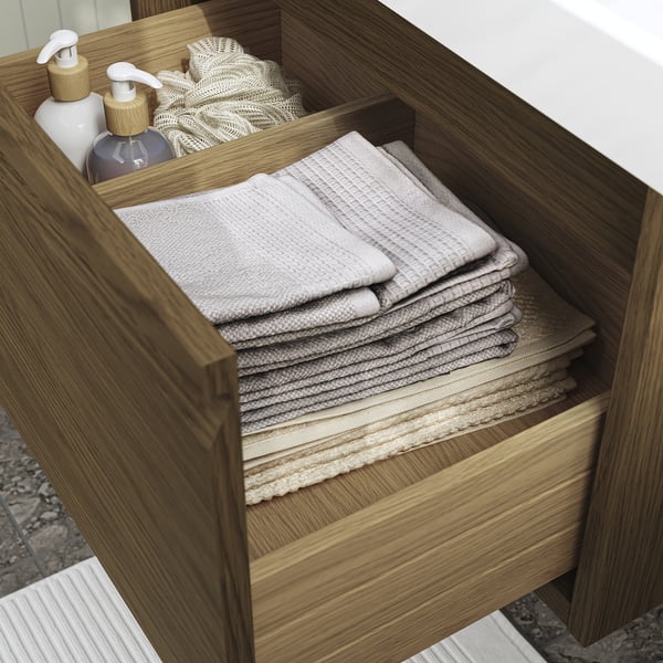 Open wooden bathroom drawer revealing neatly folded towels and soap dispensers, showcasing organized storage.