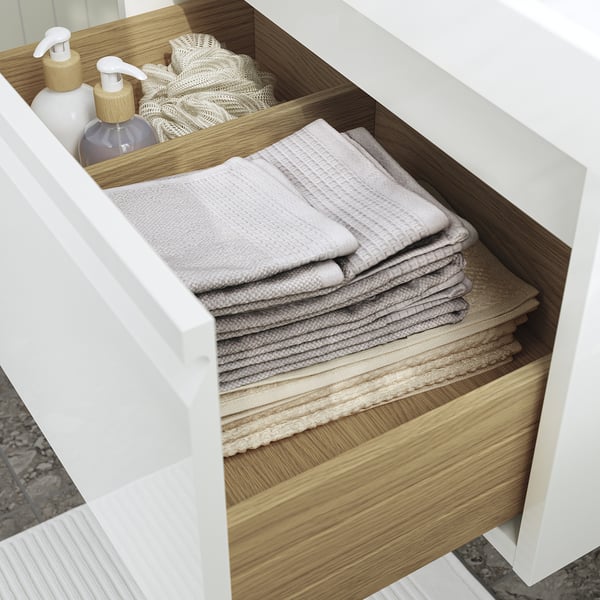 Open bathroom drawer with neatly stacked towels and soap dispensers.