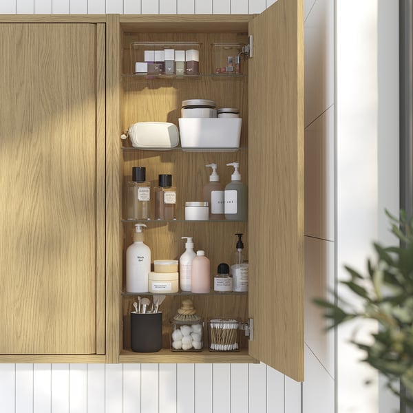 Open wooden bathroom cabinet with glass shelves holding toiletries and cosmetics.