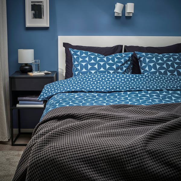 Modern bedroom with blue patterned bedding. Blue walls, grey nightstand with lamp.