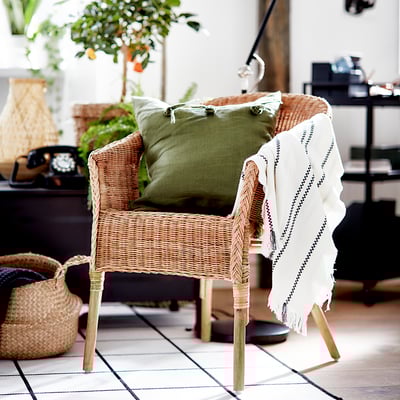 Cosy indoor scene with wicker AGEN chair, green pillow, white blanket, baskets, and plants.