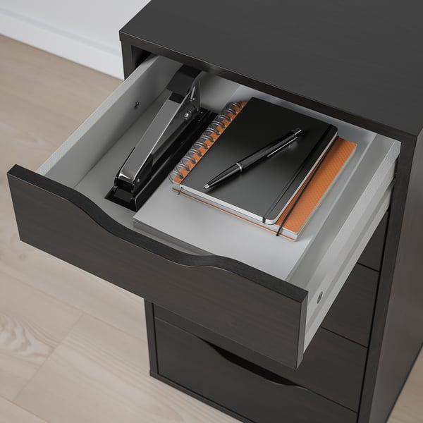 A desk drawer with a black binder, pen, and notebooks. The drawer slides are visible, showing how it opens smoothly.