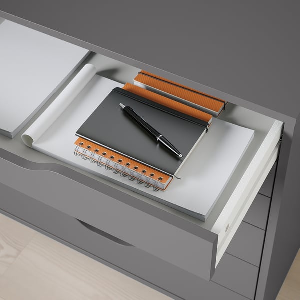 Desk drawer with notebook, pen, and paper roll, showcasing organised workspace with drawer stops for safety.