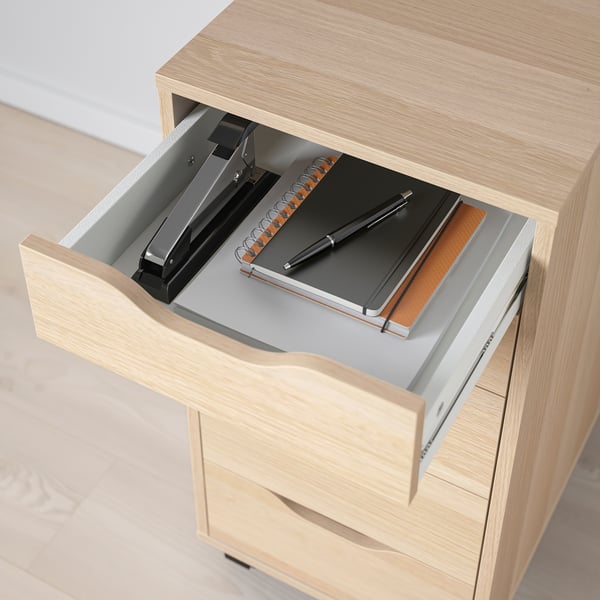 Open wooden drawer showing a stapler, notebook, and pen, illustrating organised storage.