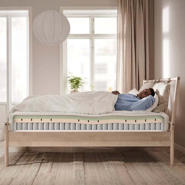 Person sleeping on ÅNNELAND hybrid mattress in well-lit room.