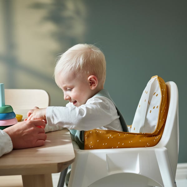 Baby in high chair with inflatable support cushion, playing with colourful blocks on a table.