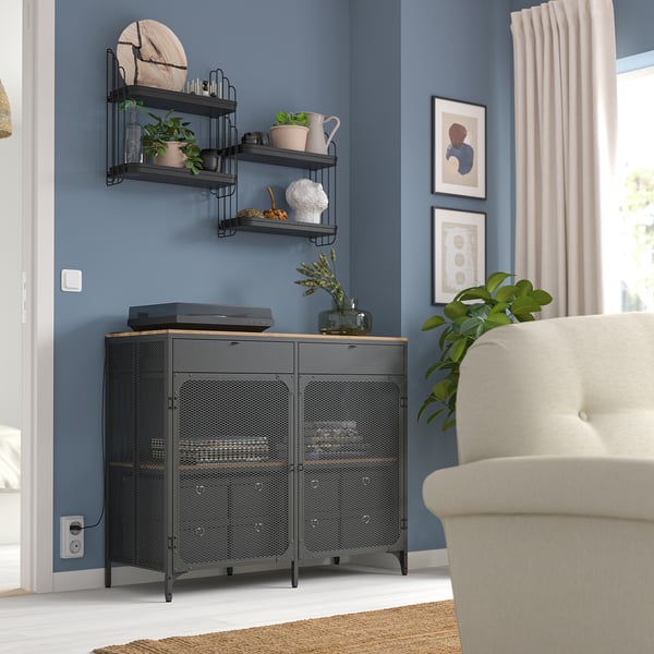 Black metal shelf with plants, decor, and electronics, fitting in room corner next to beige armchair.