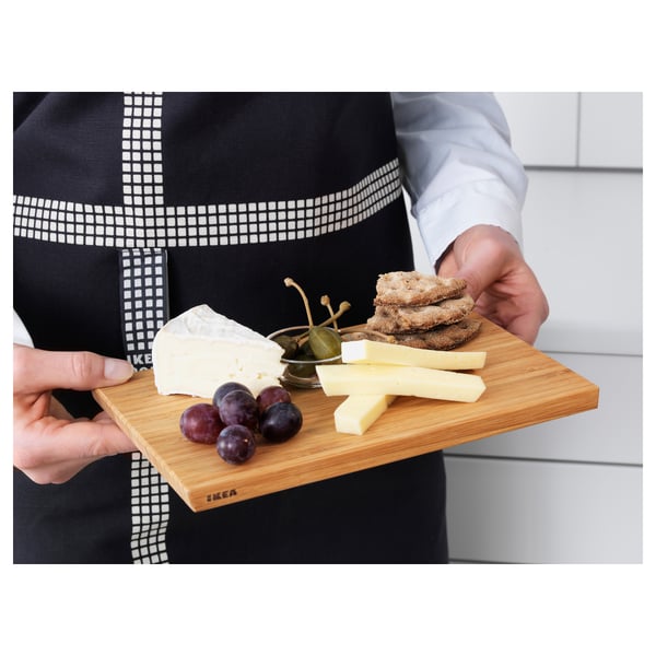 Person holding a wooden tray with cheese, crackers, and grapes.