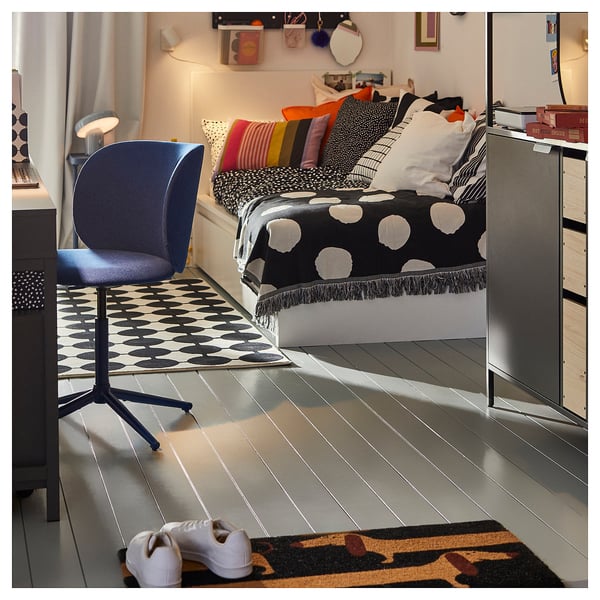 Modern bedroom with black and white bedding, colourful pillows, blue chair, and patterned rug.