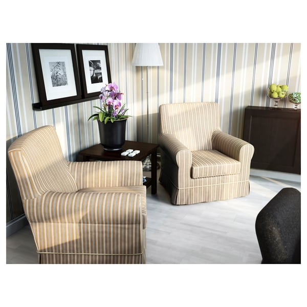 Modern living room with striped armchairs, wood table, and lamp. Decor includes photos, orchids, and fruit bowl.