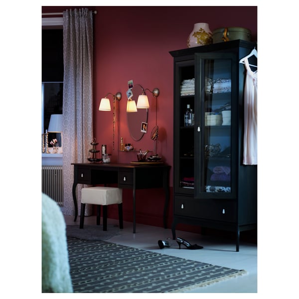 Cosy room with black dressing table, mirror, stool, and storage cabinet. Pink walls, patterned rug, and soft lighting.