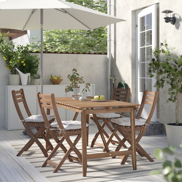 Patio with acacia table, folding chairs, striped rug, and plants on wooden deck.