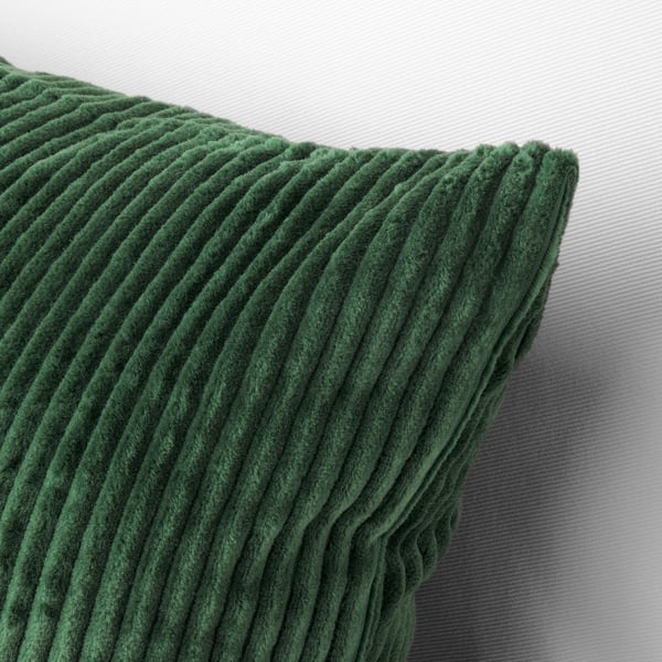 Green corduroy cushion cover on a bed. Texture and stitching detail visible.