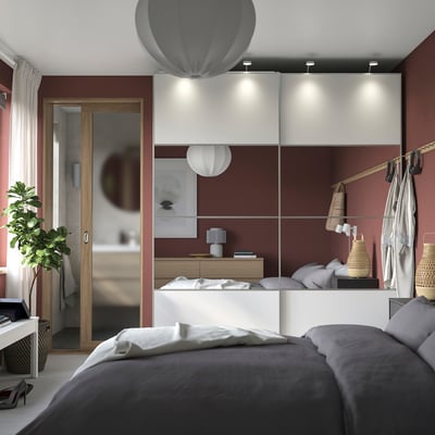 Modern red bedroom with grey bed, table lamp, mirrored wardrobe, hanging lights, and plant.