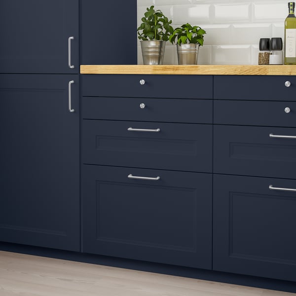 AXSTAD blue kitchen cabinets, modern design with silver handles. Three potted plants sit on wooden countertop.