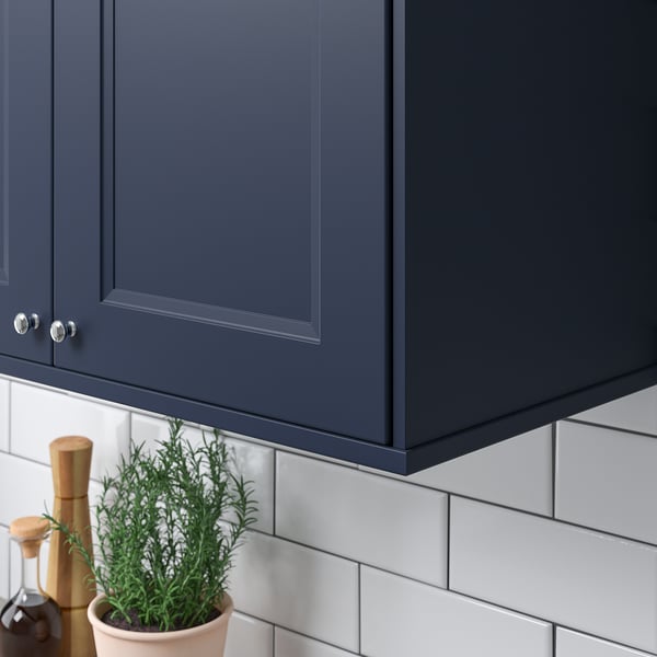 Dark grey kitchen cabinet with silver handles above a green plant and white tile backsplash.