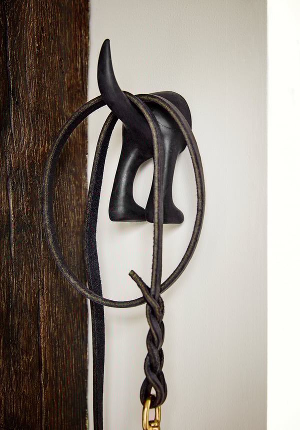 Miniature black dog hook hangs on wooden wall, securing black braided leash with gold clasp.