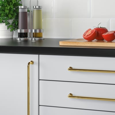 Modern kitchen with BAGGANÄS brass handles on grey drawers, featuring a cutting board with tomatoes and condiments.