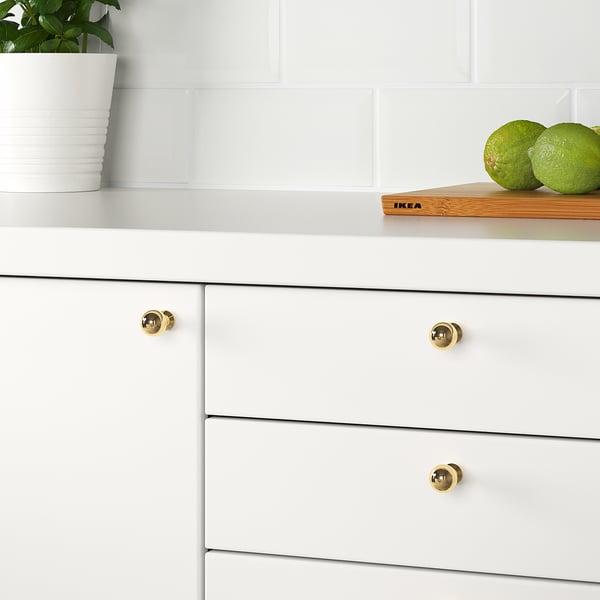 White kitchen drawers with gold knobs, one open with limes, plant nearby.