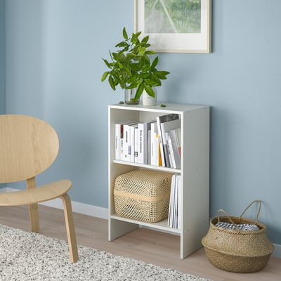 White BAGGEBO bookshelf with books and decor in a cosy corner next to a wooden chair and a woven basket.