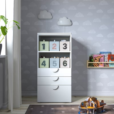 Childs room with cloud walls, storage unit, rug, bookshelf, toys, curtain, radiator, plant.