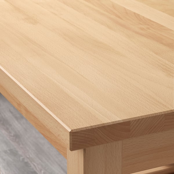A close-up of a wooden table with a smooth, light finish. The grain of the beech wood is clearly visible, highlighting its quality and craftsmanship.