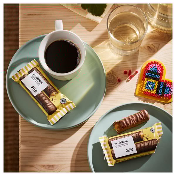 Top view of two green plates with belaning chocolate bars, one unwrapped, and a cup of coffee on a wooden table.