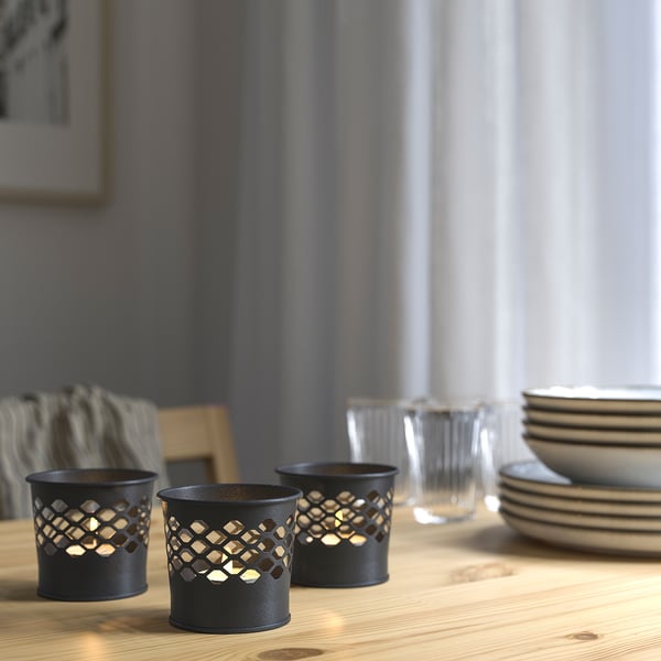 Three black metal candle holders with cut-out patterns on a wooden table, creating decorative light patterns.