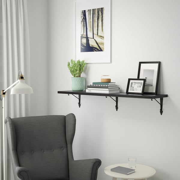 Wall shelf BERGSHULT, black. Holds books, frames & plant. Mounted high above cosy grey chair. Lightweight, slim design.