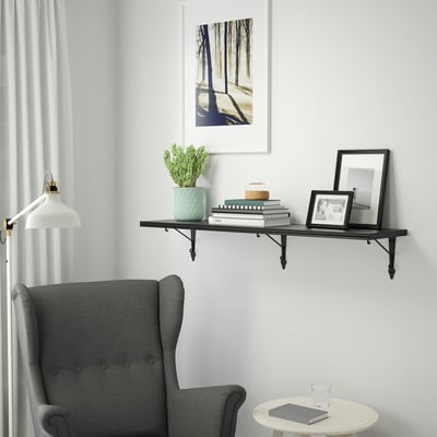Wall shelf BERGSHULT, black. Holds books, frames & plant. Mounted high above cosy grey chair. Lightweight, slim design.