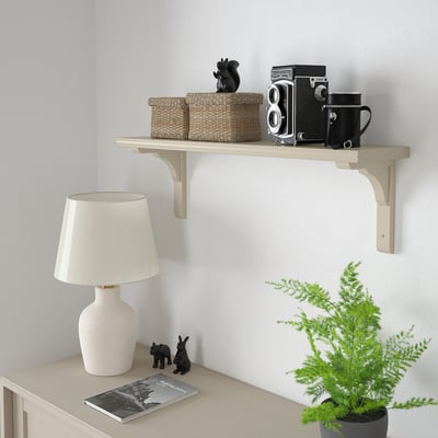 BERGSHULT shelf holds wicker baskets, vintage camera, mug, and statue. White lamp, plant, book by furniture. Beige, simple, rectangular.