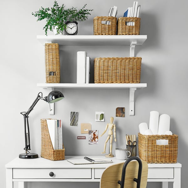 Well-organized white desk with wicker baskets, a lamp, and a plant on shelves, creating a neat, tidy workspace.