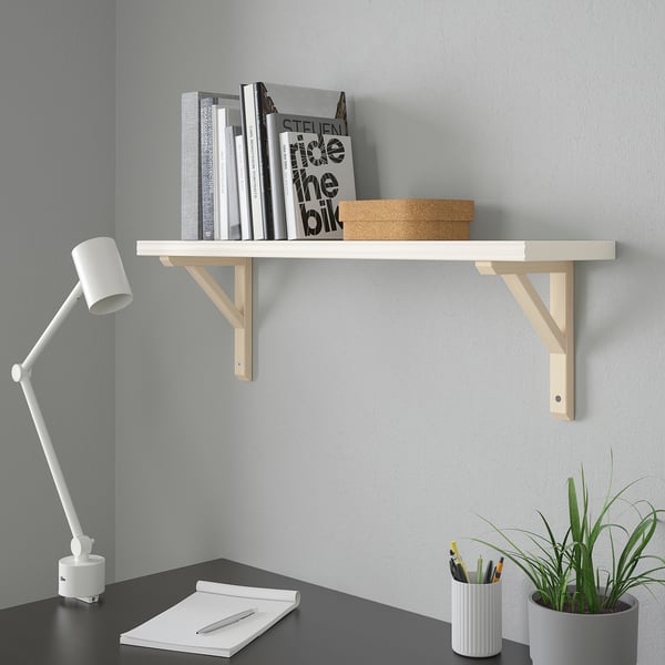 White BERGSHULT shelf above desk holding books & box, desk has lamp, notebook, pens, plant.