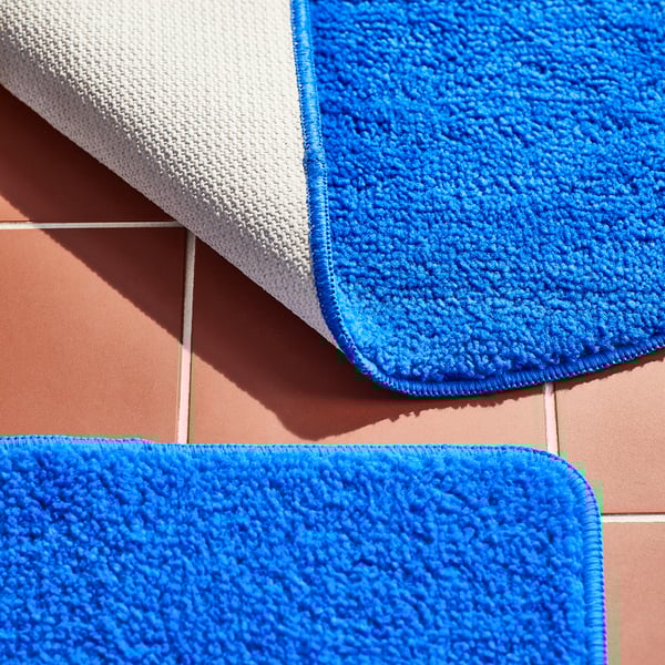 Soft, vibrant blue bathmats with textured surfaces and anti-slip backing neatly arranged on pink tiles.
