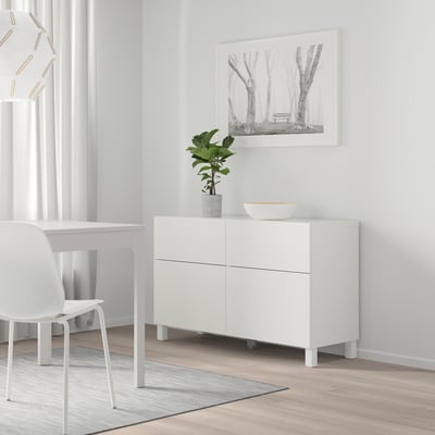 Minimalistic white BESTÅ cabinet with 2 drawers, paired with a white dining set and plant. Wall art shows a serene forest.