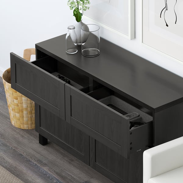 Black BESTÅ sideboard with adjustable shelves and drawers, one drawer open showing remote control holder.