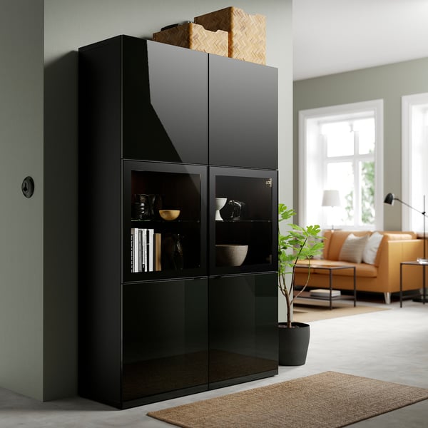 Black BESTÅ cabinet with glass doors near green wall and window, brown sofa and lamp.