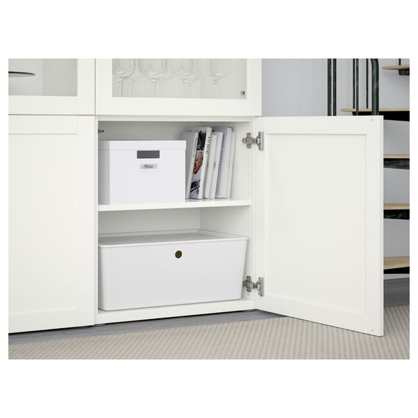 White cabinet with adjustable shelves; one shelf has a white storage box and magazines. The door has soft-closing hinges.