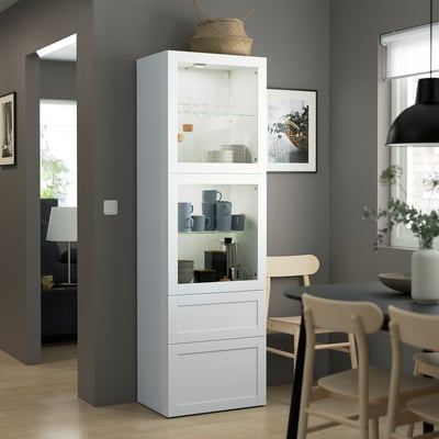 Modern BESTÅ white storage unit with glass doors between chairs.