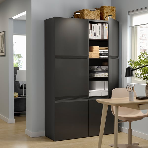Modern living room with black BESTÅ storage unit, white chairs, wooden floor, and grey walls. Books and baskets are stored on open shelves.