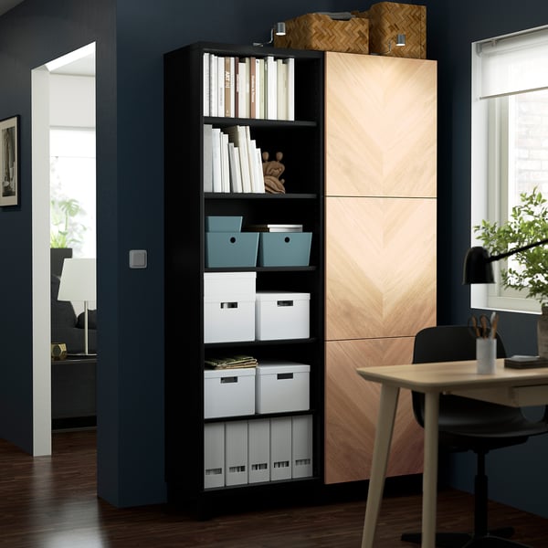 Black BESTÅ storage unit with open shelves and closed cabinets, organised boxes against dark blue wall.