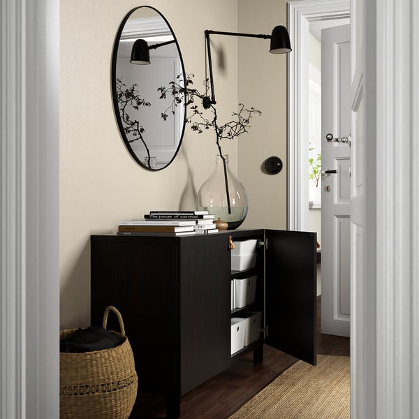 Modern BESTÅ cabinet with open door, storage boxes, vase, books, basket, and mirror.