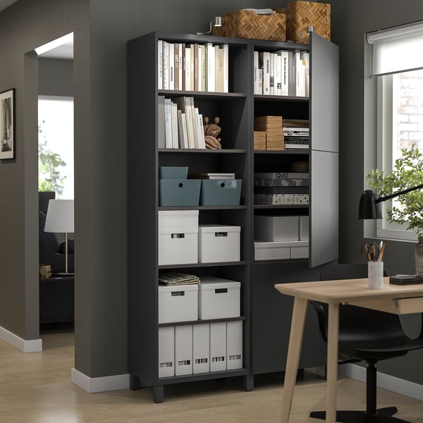Black BESTÅ storage unit with open/closed compartments, books, beside desk & chair in home office.