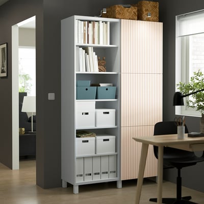 A large BESTÅ storage unit with shelves and doors in a room, beside a window and grey pillar.
