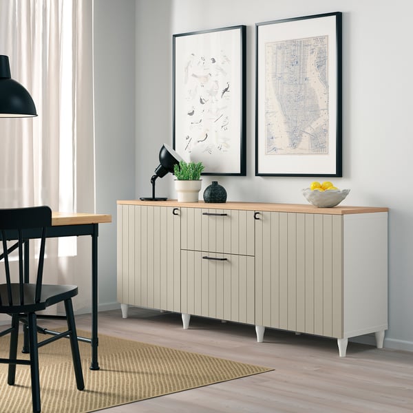 Modern living room corner with white BESTÅ sideboard, black lamp, wall art, and fruited bowl. Tall, light, clean look.