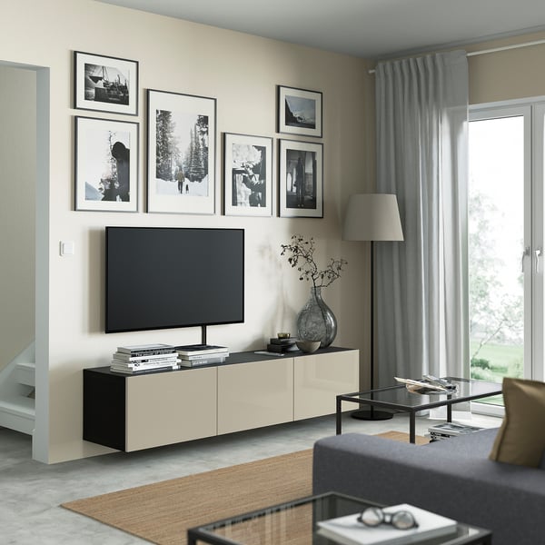 Modern living room with BESTÅ tv stand, flat-screen tv, books, vase, wall art, glass coffee table, dark grey sofa, lamp, and grey curtains.