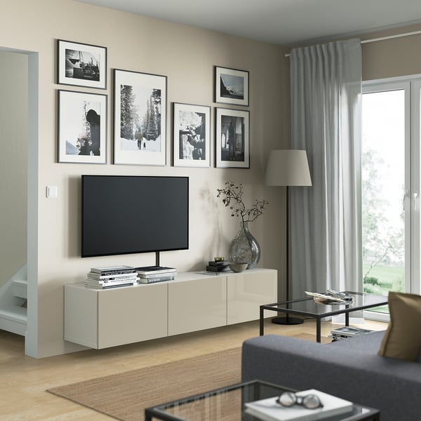 Modern living room with BESTÅ tv bench, flat-screen tv, black/white photos, glass coffee table, grey sofa, tall lamp, large window with grey curtains.