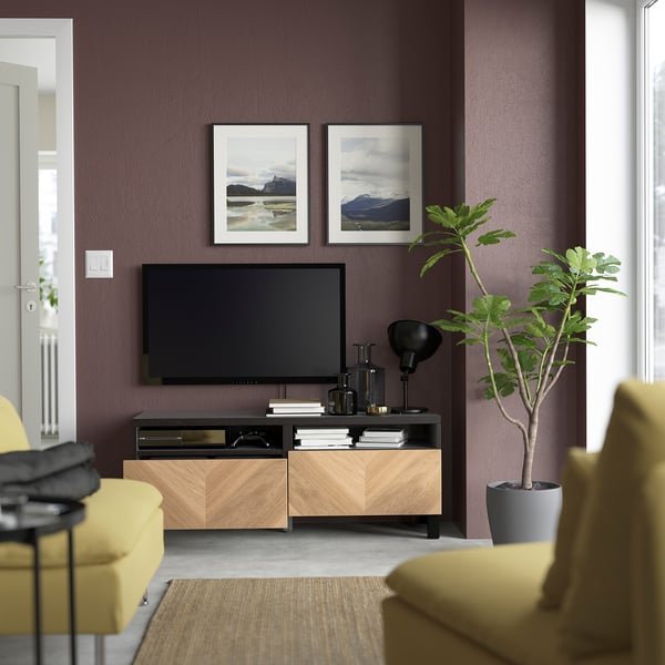 Modern living room with purple walls, flat-screen tv on wooden unit with two drawers, yellow couch, plants, and nature frames.